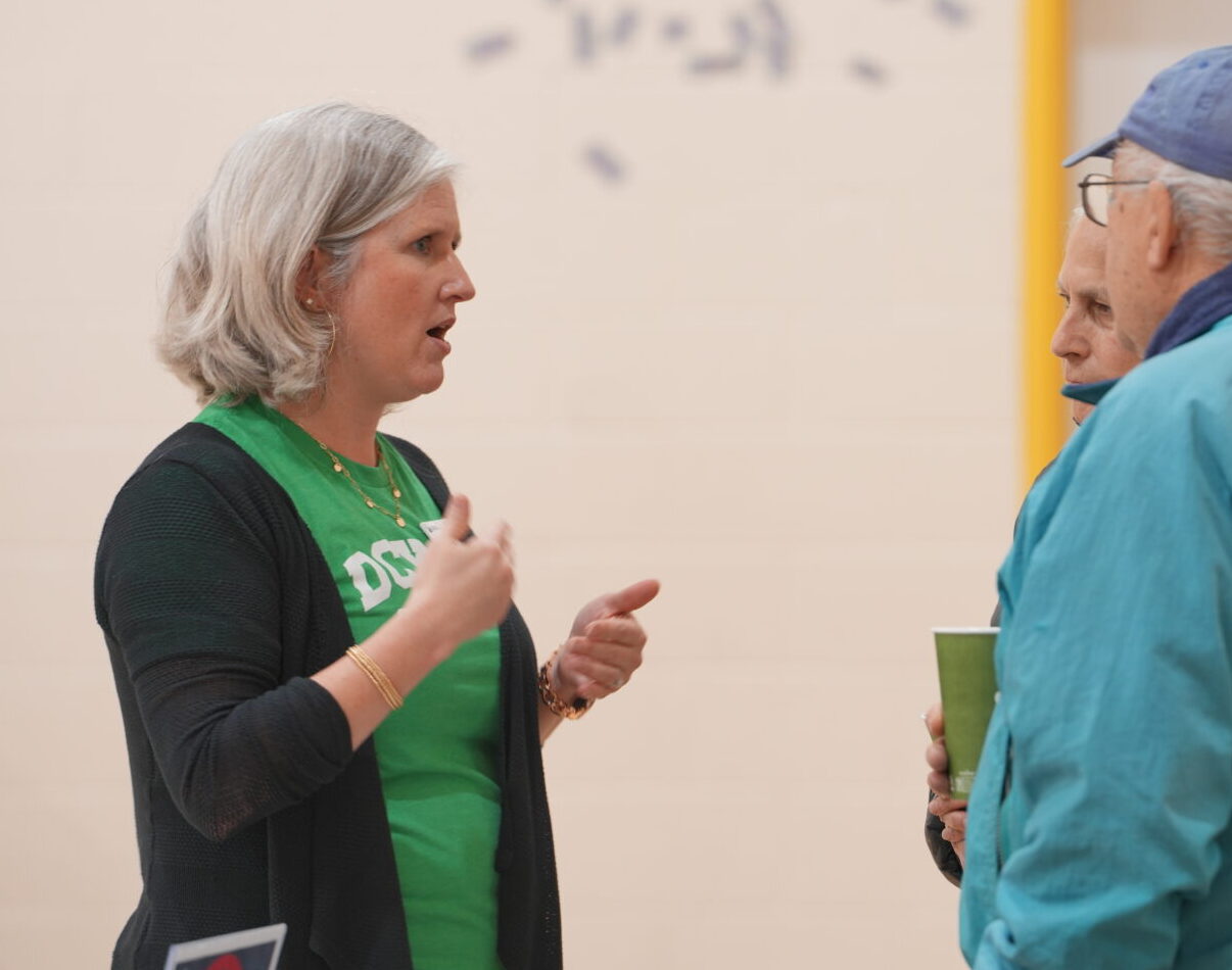 KellyAnn Nelson of DCYOP, wearing a green shirt and black cardigan, speaks animatedly with two adults in a casual indoor setting.